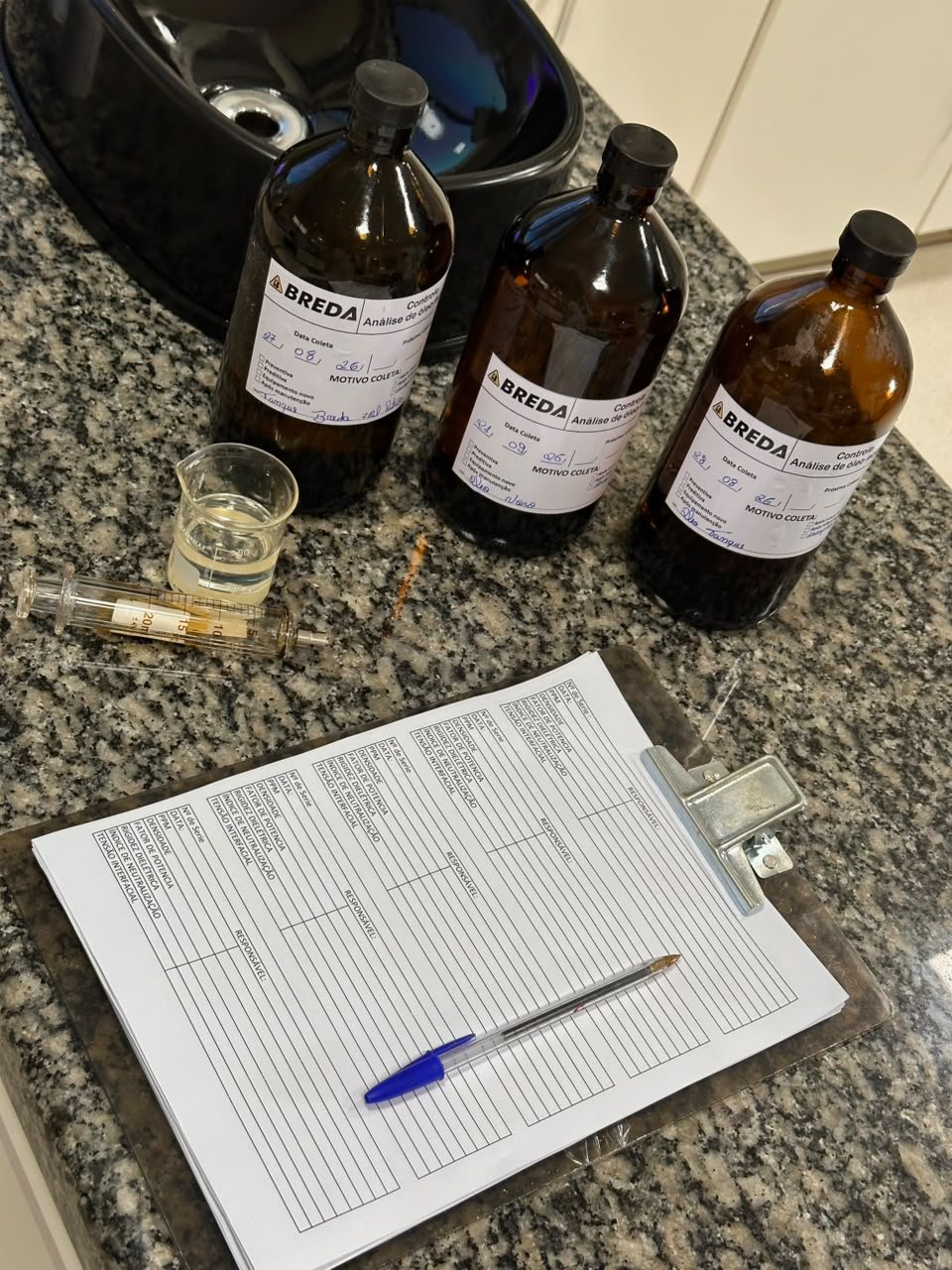Frascos âmbar com etiqueta de controle de análise de óleo da BREDA, seringa de coleta e a ficha de controle sobre a bancada