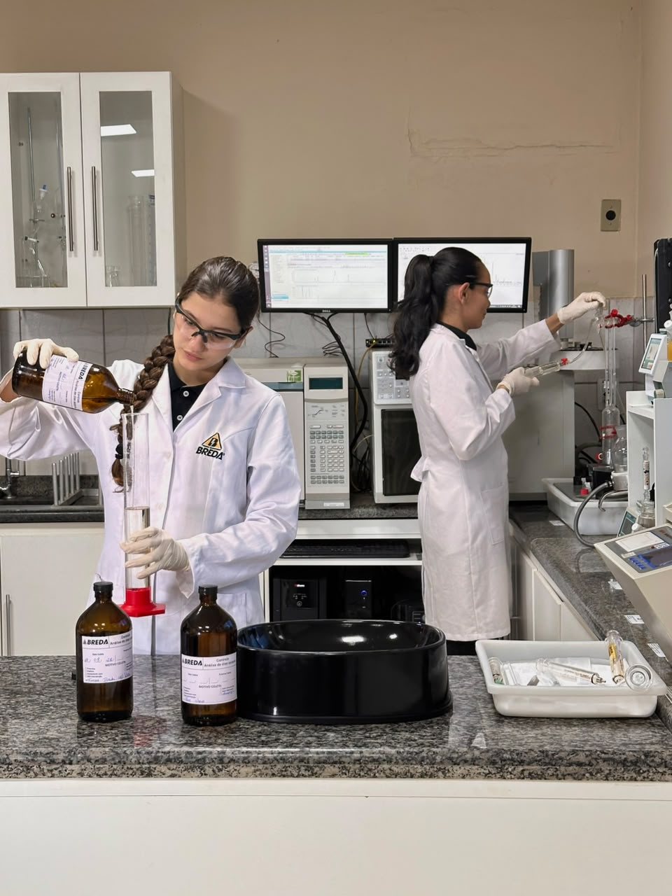 Laboratório da BREDA: duas analistas trabalhando, uma vertendo a amostra em proveta e outra na bancada