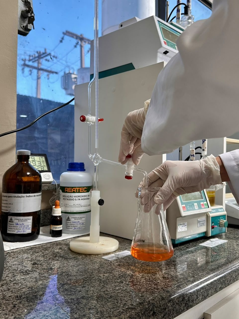Titulação em bancada de laboratório: bureta com hidróxido de potássio e erlenmeyer com a amostra de óleo no ponto de viragem