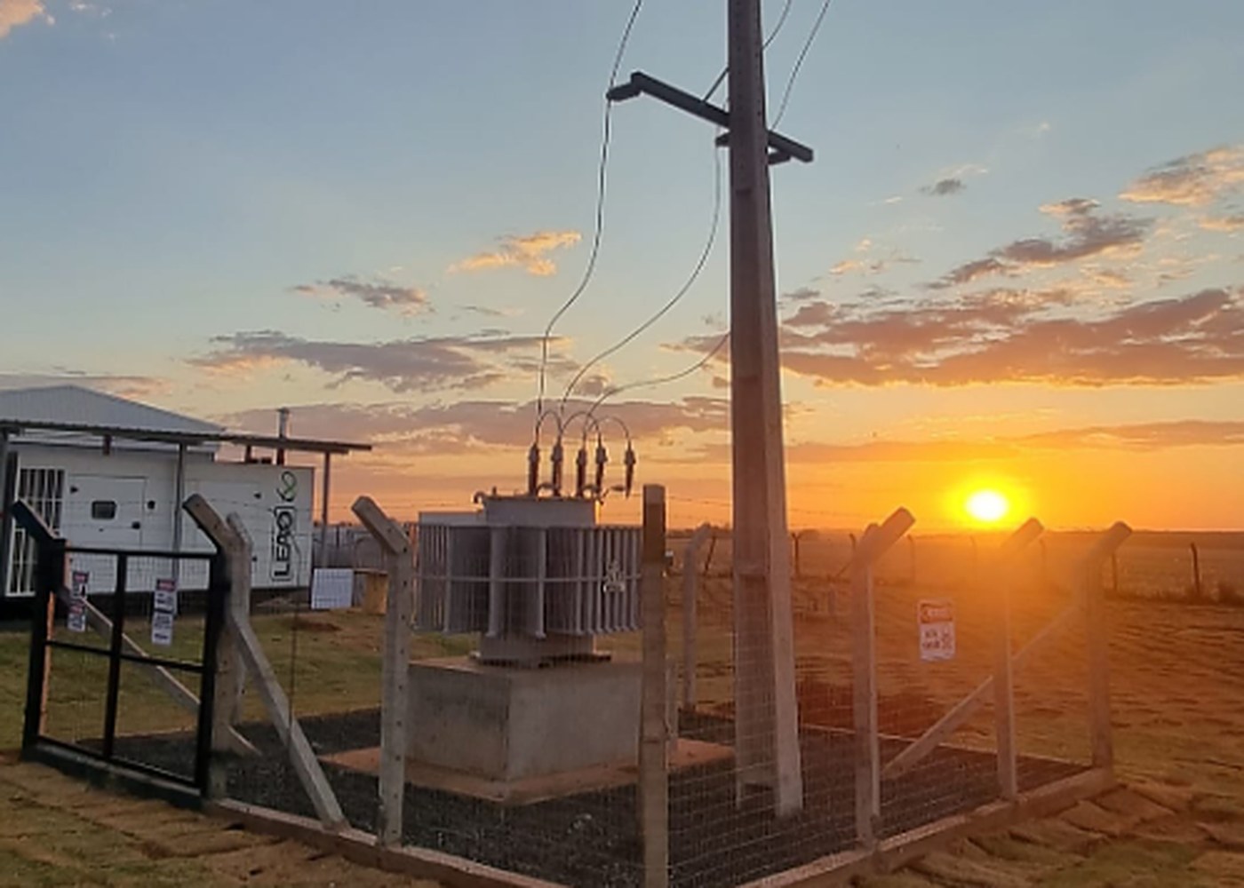 Transformador montado pela BREDA sobre base de concreto, em área cercada junto ao poste, ao pôr do sol