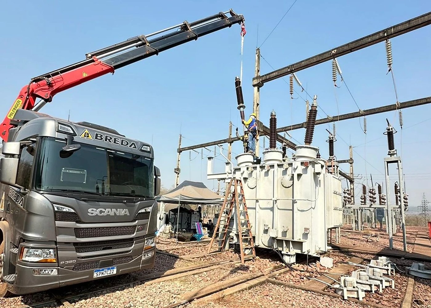 Caminhão munck da BREDA e técnico em altura instalando bucha de transformador numa subestação