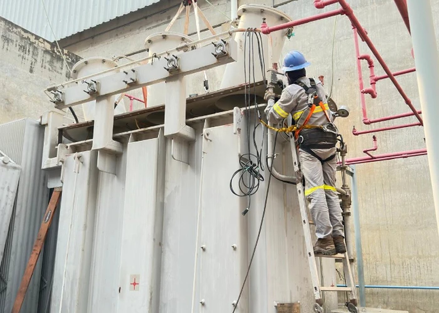Técnico com cinto de segurança em escada, fazendo tratamento de óleo em transformador de força instalado