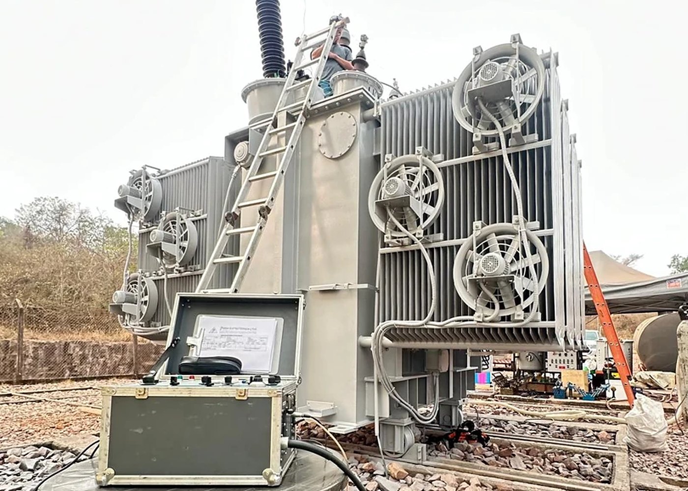 Técnico da BREDA no alto de um transformador de força em subestação, com a mala de ensaios montada em primeiro plano